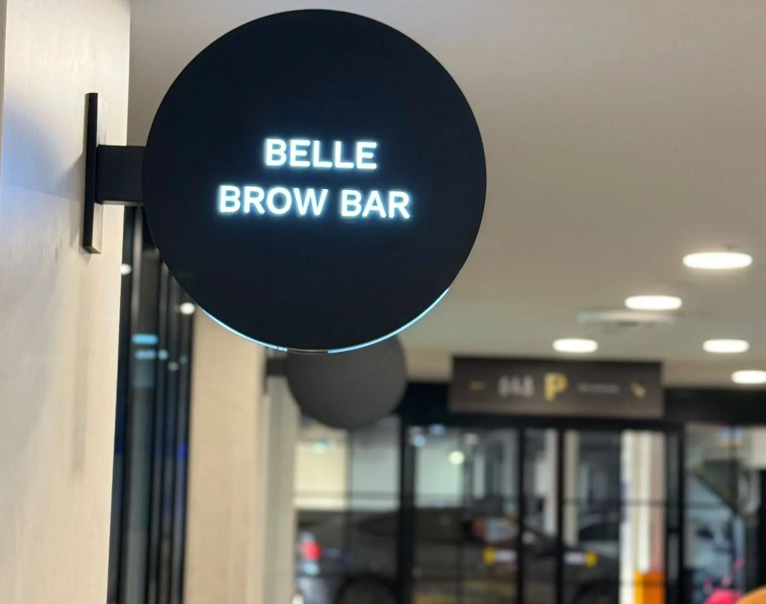 Illuminated Belle Brow Bar sign glowing white in the Acland Court walkway